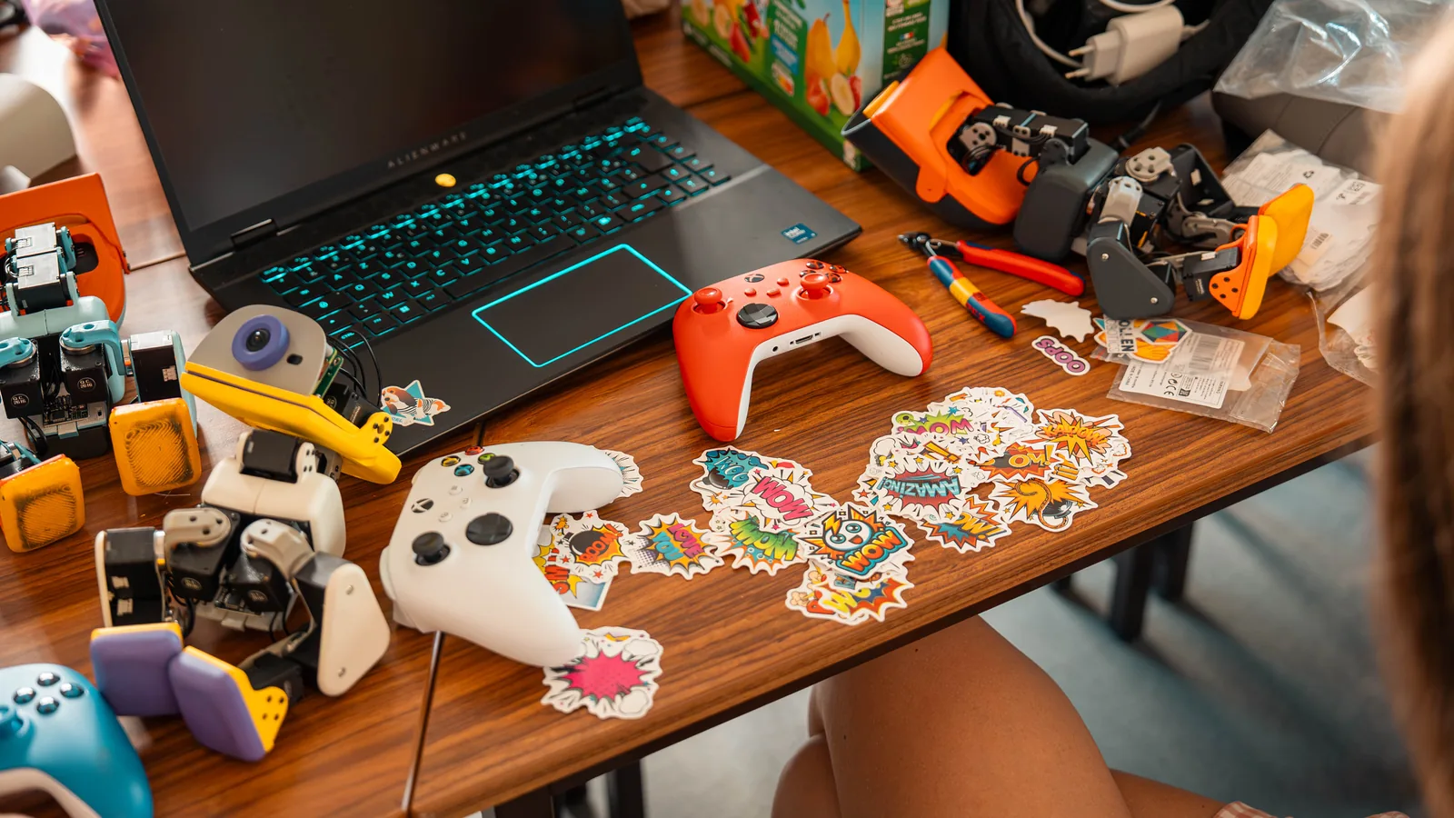 A desk with a laptop, game controllers, Microduck parts in several colors and a sheet of stickers